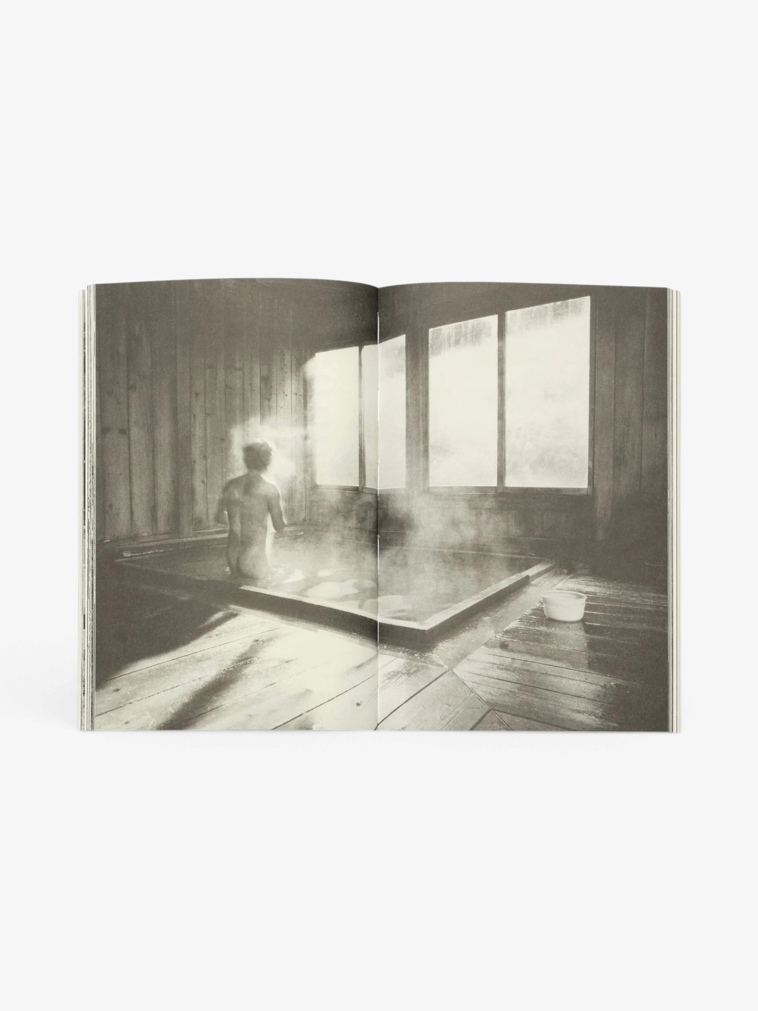 Sommer Undesigning the Bath book open to a black and white photograph of a person bathing in a steamy wooden room